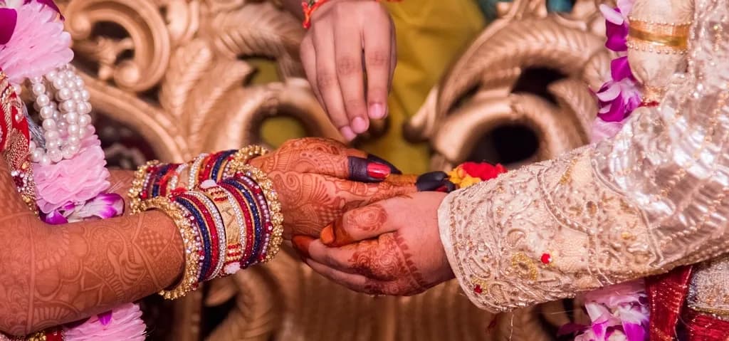 A couple's hands joined during the wedding ceremony, with mehendi and bangles